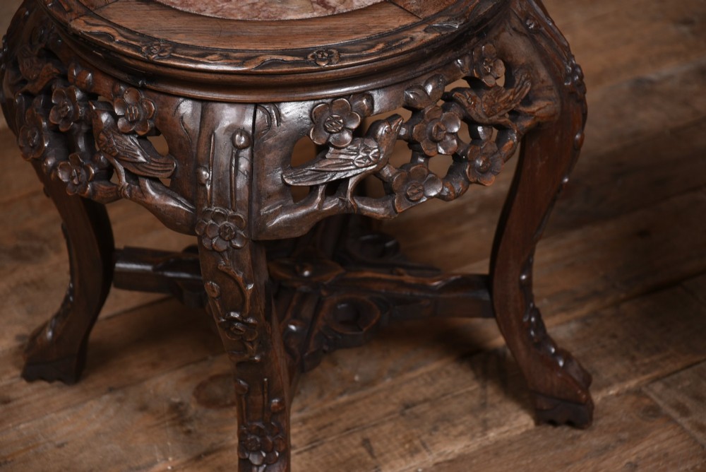 A pair of carved dark hardwood round stands featuring inset pink marble tops and pierced floral aprons supported by curved legs. View VI