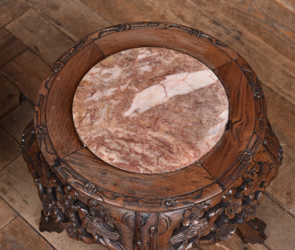 A pair of carved dark hardwood round stands featuring inset pink marble tops and pierced floral aprons supported by curved legs. View VII
