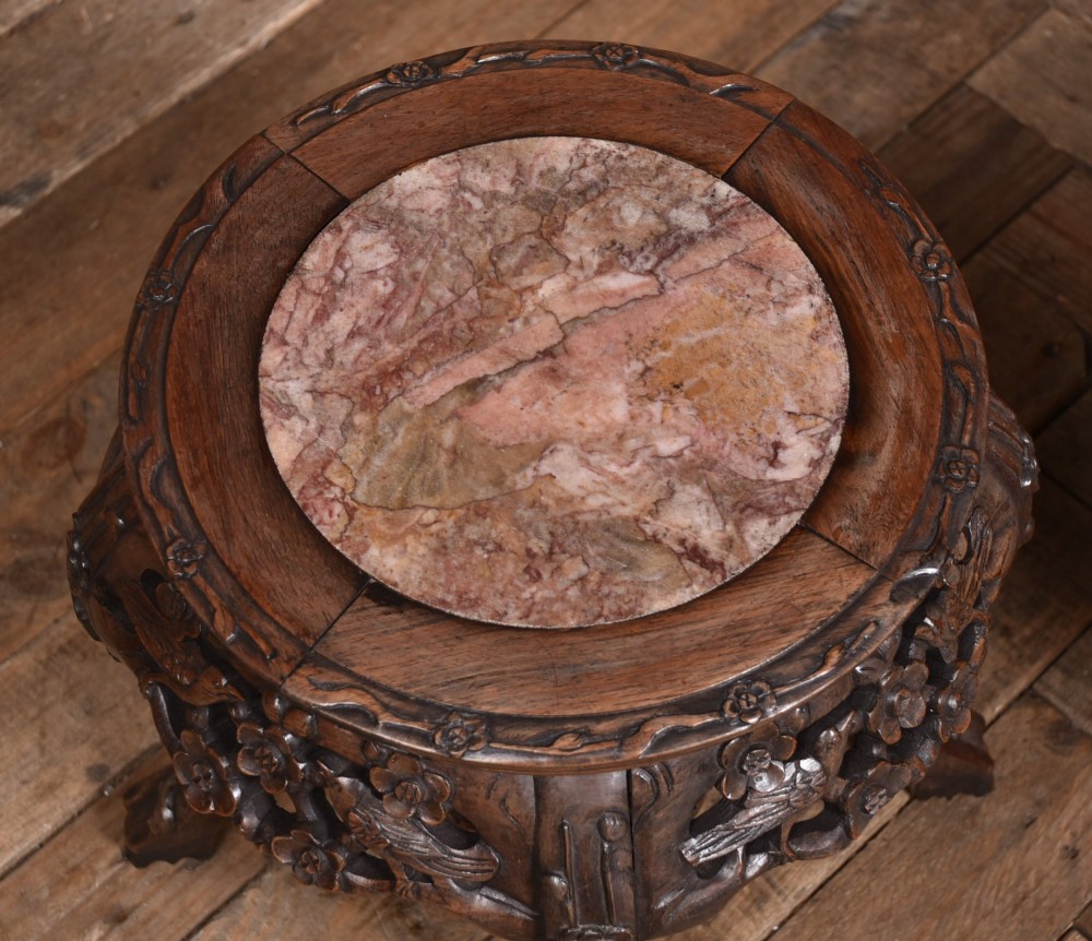 A pair of carved dark hardwood round stands featuring inset pink marble tops and pierced floral aprons supported by curved legs. View VIII