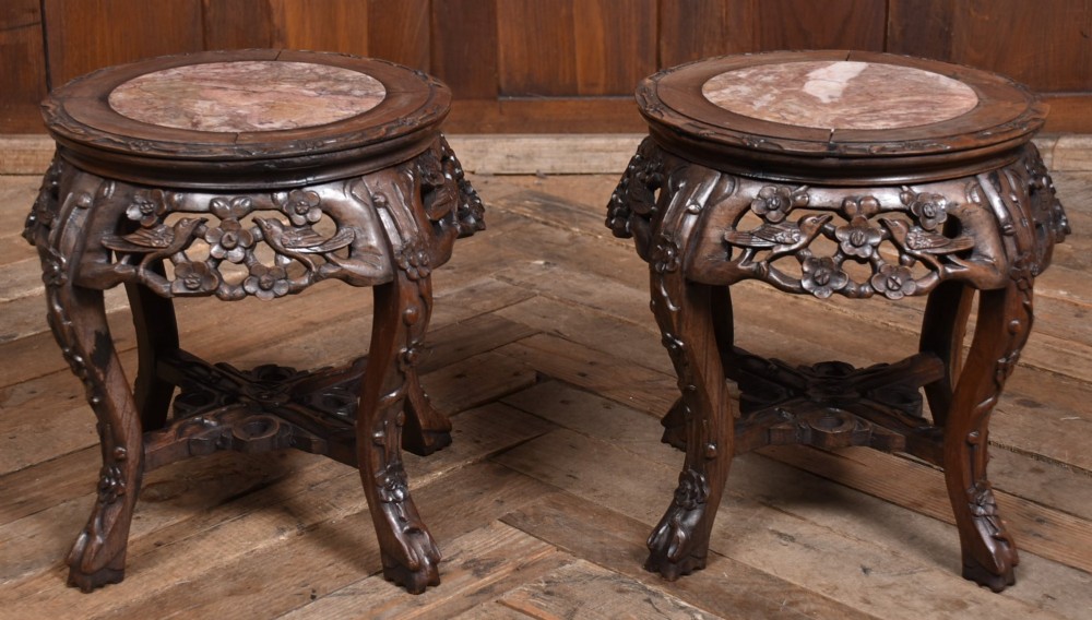 A pair of carved dark hardwood round stands featuring inset pink marble tops and pierced floral aprons supported by curved legs. View IX