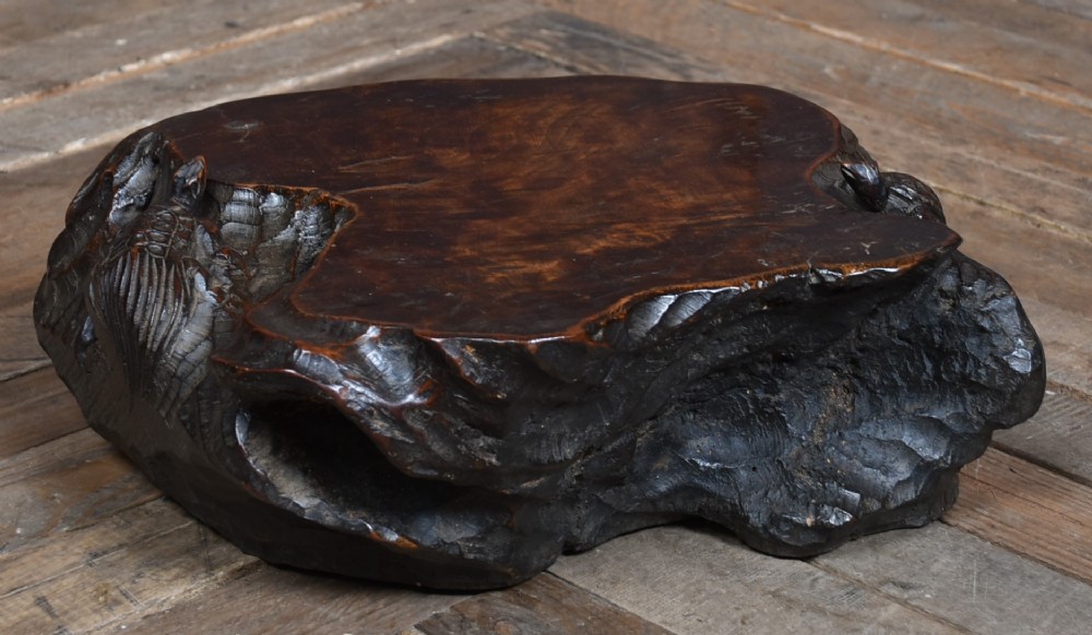A dark brown carved hardwood display stand featuring a hand-carved turtle motif along the organic natural edge.