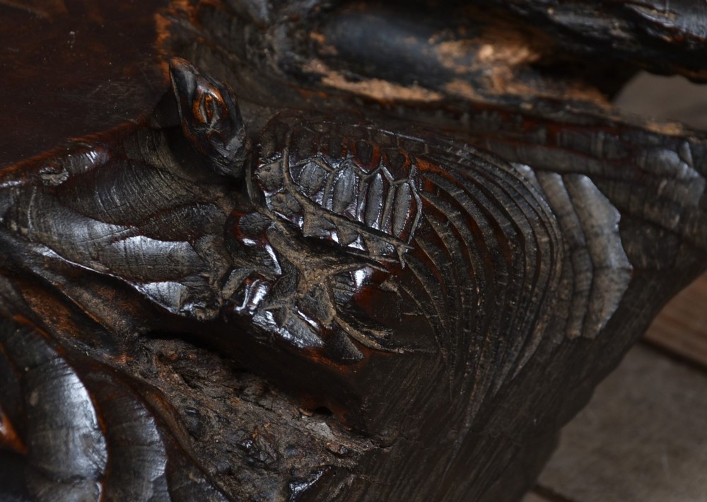 A dark brown carved hardwood display stand featuring a hand-carved turtle motif along the organic natural edge. View V