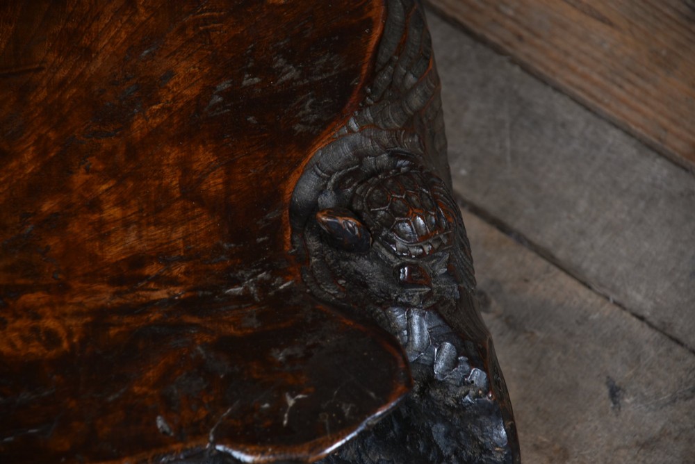 A dark brown carved hardwood display stand featuring a hand-carved turtle motif along the organic natural edge. View XII