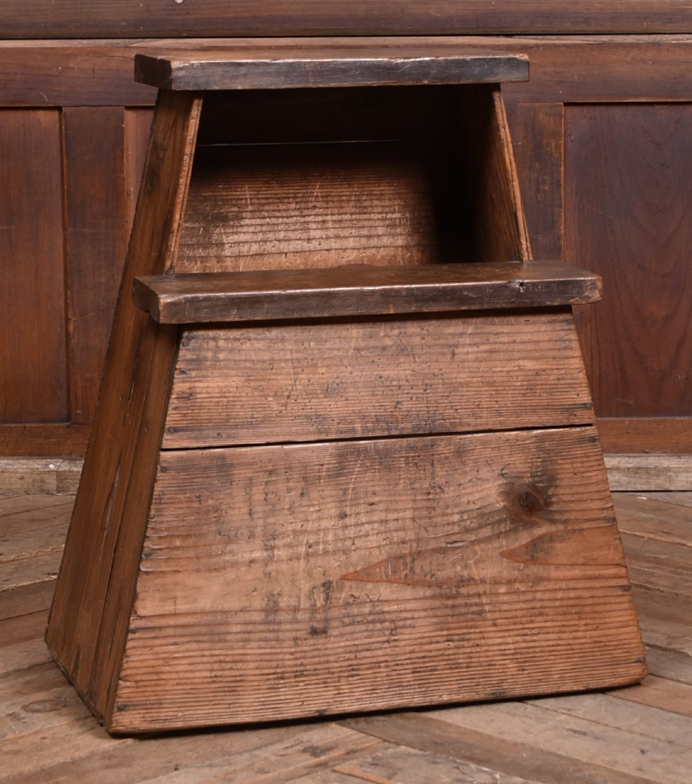 A weathered brown wooden step stool with a tapered rectangular base and an upper platform seat displaying distinct grain and patination. View II
