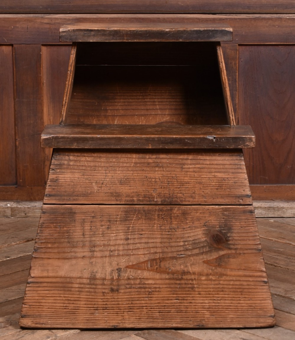 A weathered brown wooden step stool with a tapered rectangular base and an upper platform seat displaying distinct grain and patination. View III