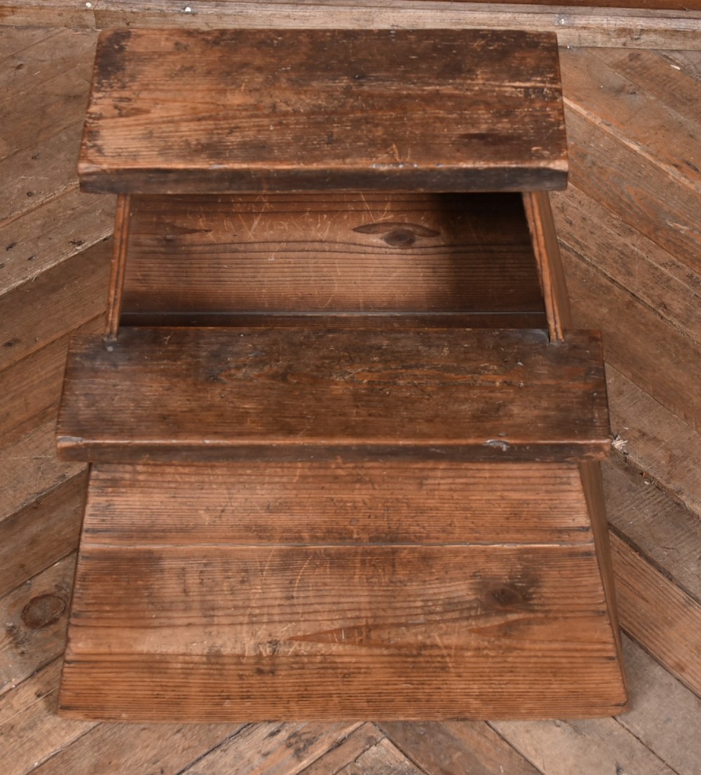 A weathered brown wooden step stool with a tapered rectangular base and an upper platform seat displaying distinct grain and patination. View VII