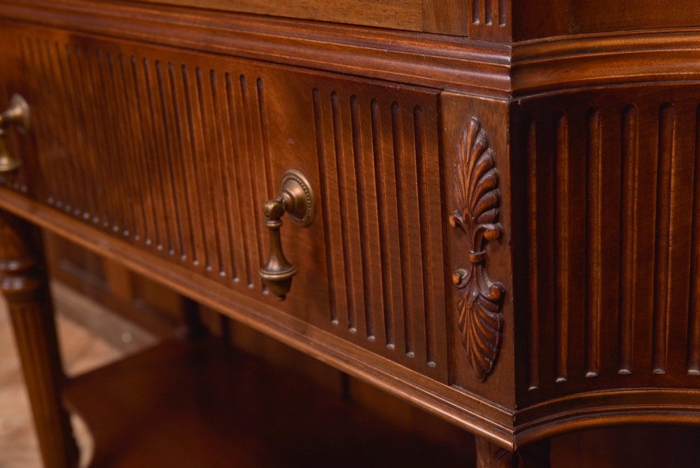 An Edwardian mahogany display cabinet featuring geometric marquetry inlay along the frieze, astragal glazed glass doors, an under-tier shelf, and turned legs. View V