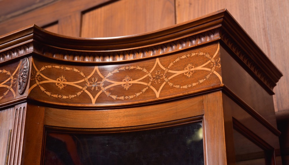 An Edwardian mahogany display cabinet featuring geometric marquetry inlay along the frieze, astragal glazed glass doors, an under-tier shelf, and turned legs. View VI