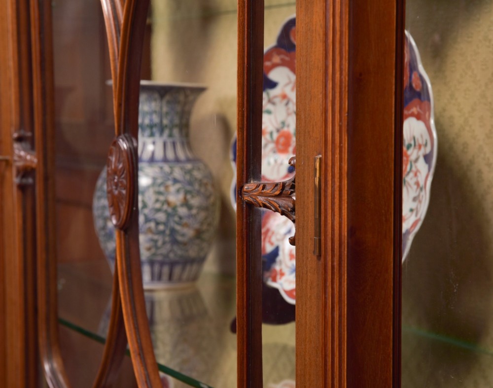 An Edwardian mahogany display cabinet featuring geometric marquetry inlay along the frieze, astragal glazed glass doors, an under-tier shelf, and turned legs. View VII