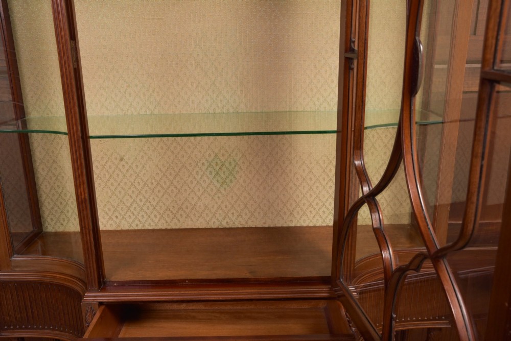 An Edwardian mahogany display cabinet featuring geometric marquetry inlay along the frieze, astragal glazed glass doors, an under-tier shelf, and turned legs. View X