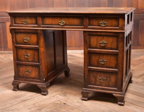 An Edwardian walnut pedestal desk featuring nine drawers with brass swan-neck handles, panelled sides, and bracket feet.