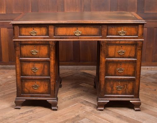An Edwardian walnut pedestal desk featuring nine drawers with brass swan-neck handles, panelled sides, and bracket feet. View III