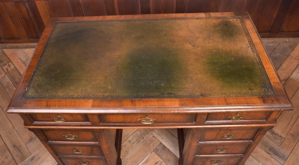 An Edwardian walnut pedestal desk featuring nine drawers with brass swan-neck handles, panelled sides, and bracket feet. View IV