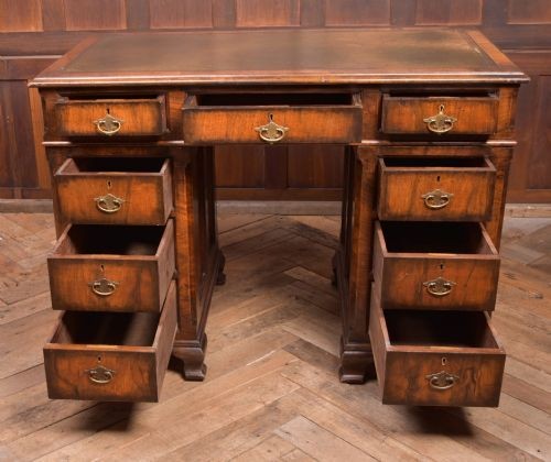 An Edwardian walnut pedestal desk featuring nine drawers with brass swan-neck handles, panelled sides, and bracket feet. View V