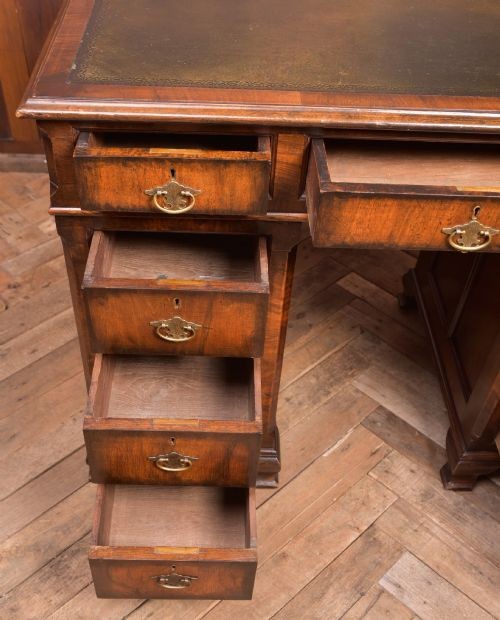 An Edwardian walnut pedestal desk featuring nine drawers with brass swan-neck handles, panelled sides, and bracket feet. View VI
