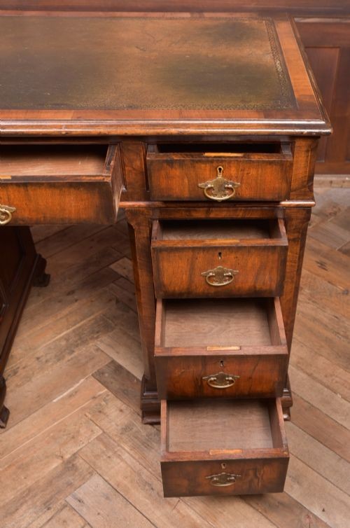 An Edwardian walnut pedestal desk featuring nine drawers with brass swan-neck handles, panelled sides, and bracket feet. View VII