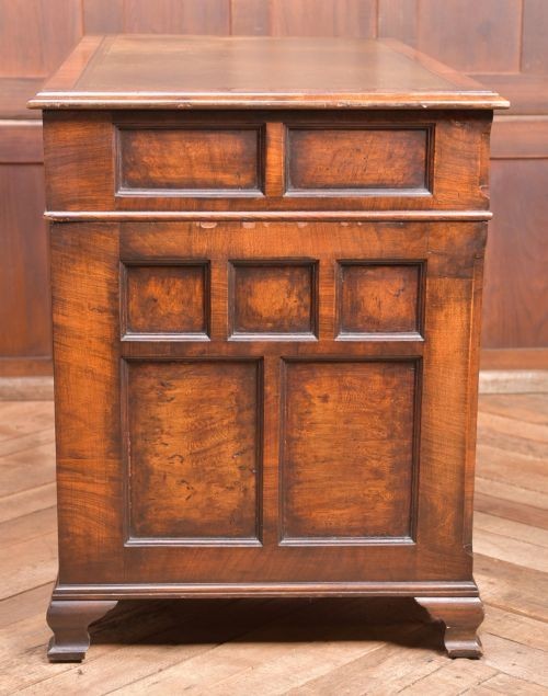 An Edwardian walnut pedestal desk featuring nine drawers with brass swan-neck handles, panelled sides, and bracket feet. View IX
