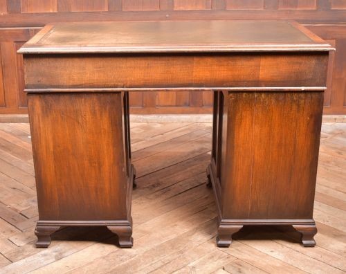 An Edwardian walnut pedestal desk featuring nine drawers with brass swan-neck handles, panelled sides, and bracket feet. View XII