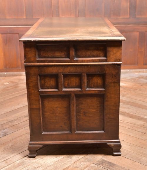 An Edwardian walnut pedestal desk featuring nine drawers with brass swan-neck handles, panelled sides, and bracket feet. View XIII