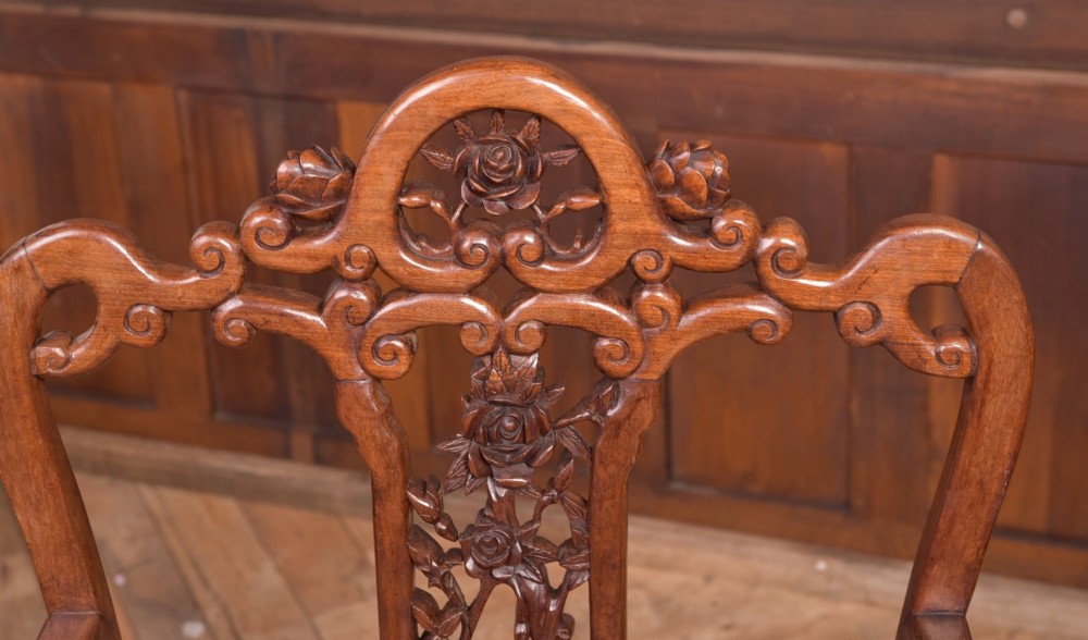 A pair of dark warm brown Chinese hardwood armchairs featuring intricately carved floral back splats, openwork scroll aprons, and sculpted legs. View II