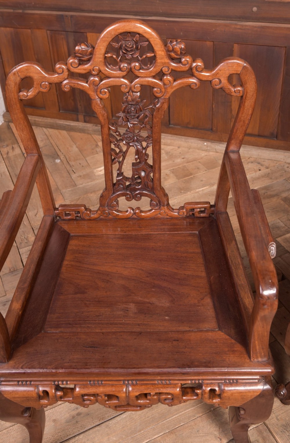 A pair of dark warm brown Chinese hardwood armchairs featuring intricately carved floral back splats, openwork scroll aprons, and sculpted legs. View III