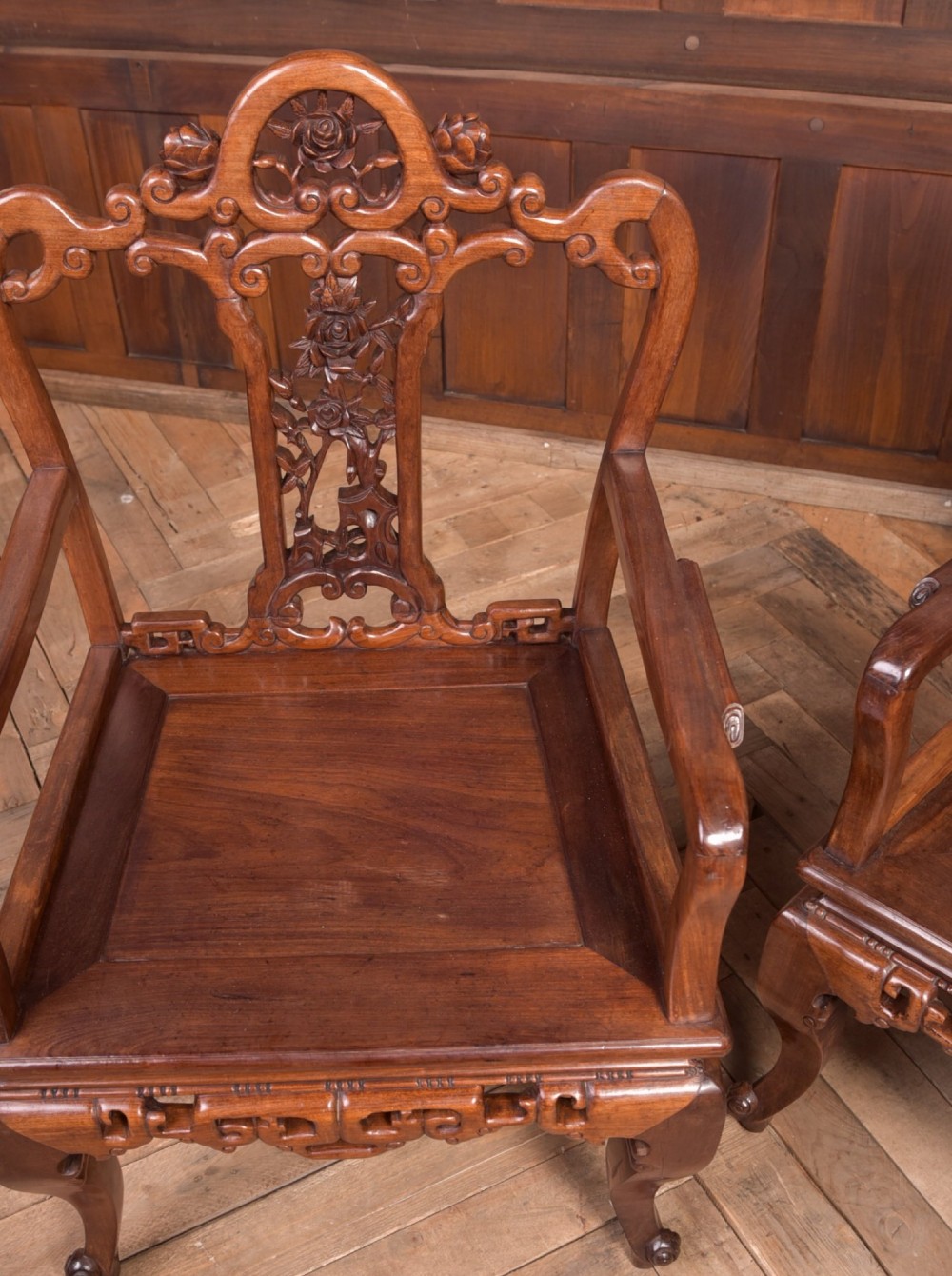 A pair of dark warm brown Chinese hardwood armchairs featuring intricately carved floral back splats, openwork scroll aprons, and sculpted legs. View IV