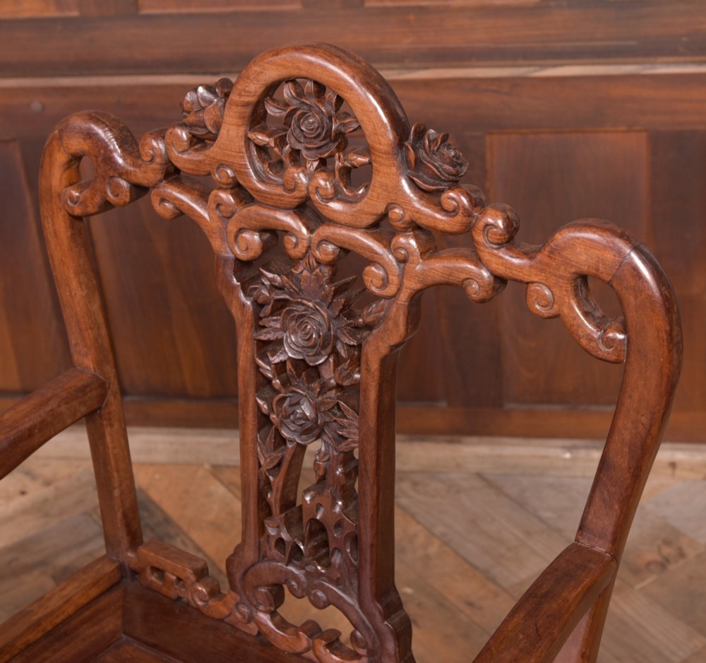 A pair of dark warm brown Chinese hardwood armchairs featuring intricately carved floral back splats, openwork scroll aprons, and sculpted legs. View V