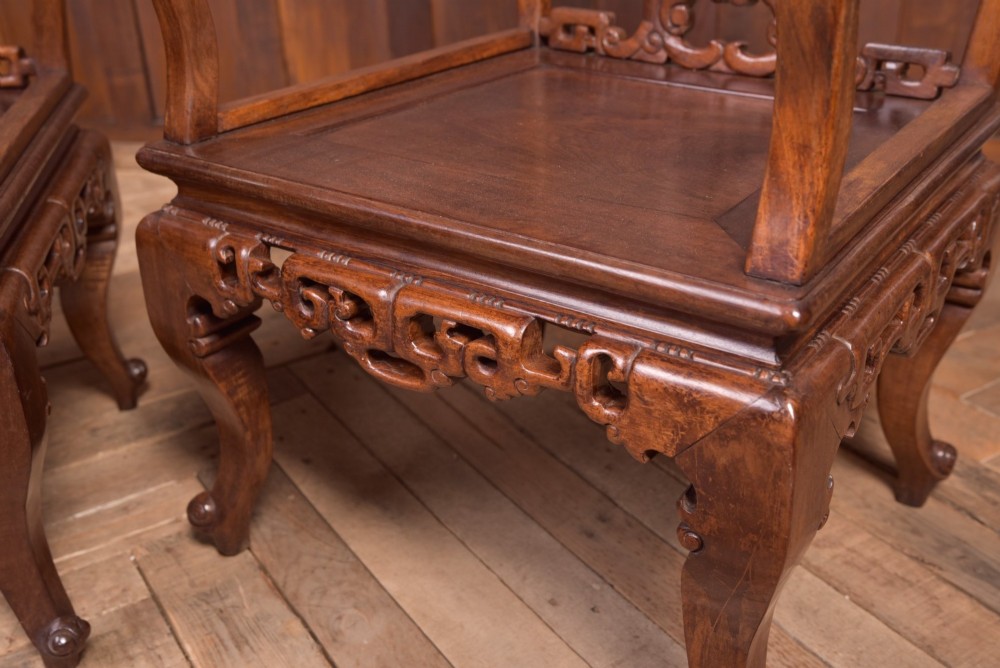 A pair of dark warm brown Chinese hardwood armchairs featuring intricately carved floral back splats, openwork scroll aprons, and sculpted legs. View VI