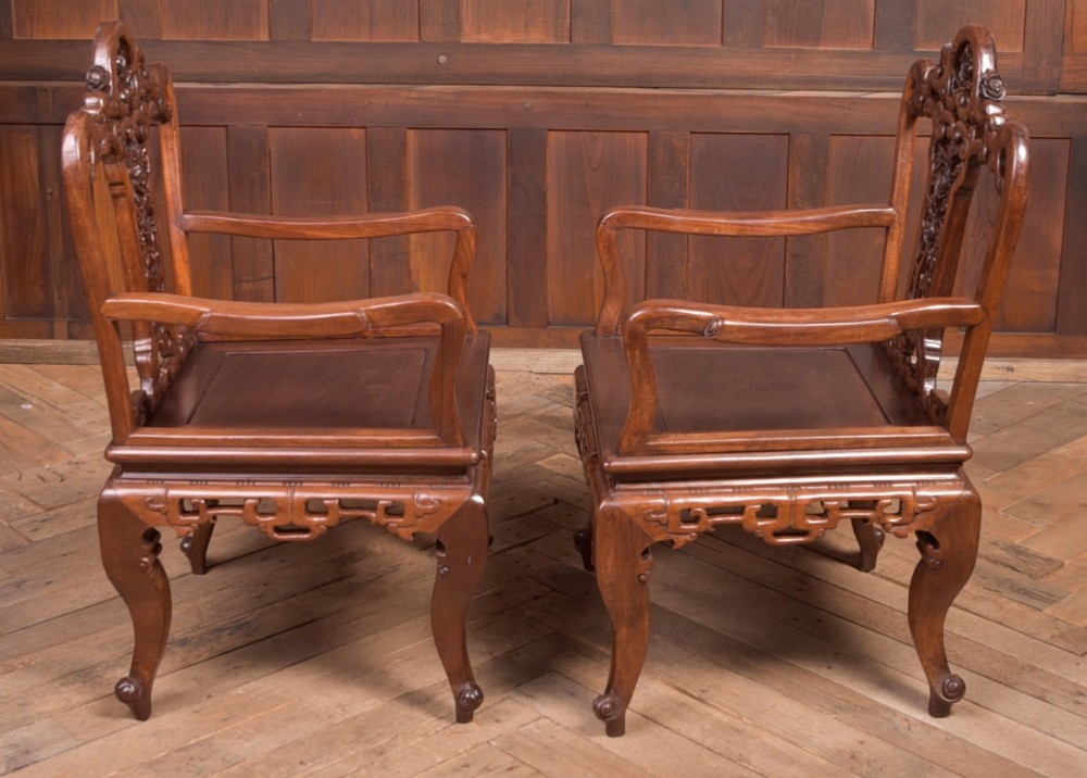 A pair of dark warm brown Chinese hardwood armchairs featuring intricately carved floral back splats, openwork scroll aprons, and sculpted legs. View VII