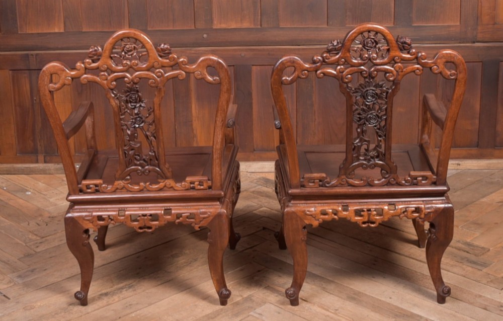 A pair of dark warm brown Chinese hardwood armchairs featuring intricately carved floral back splats, openwork scroll aprons, and sculpted legs. View VIII