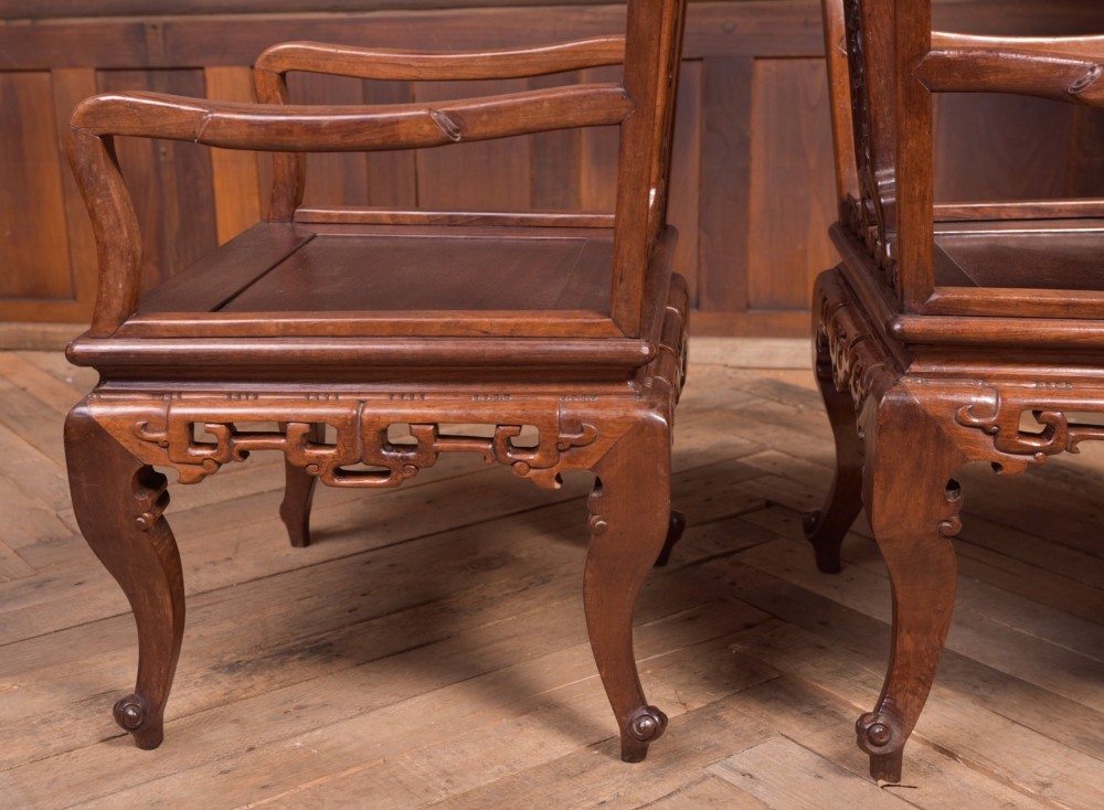 A pair of dark warm brown Chinese hardwood armchairs featuring intricately carved floral back splats, openwork scroll aprons, and sculpted legs. View IX
