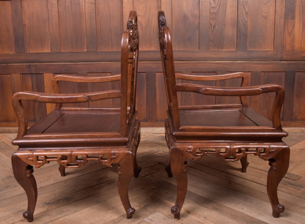 A pair of dark warm brown Chinese hardwood armchairs featuring intricately carved floral back splats, openwork scroll aprons, and sculpted legs. View X
