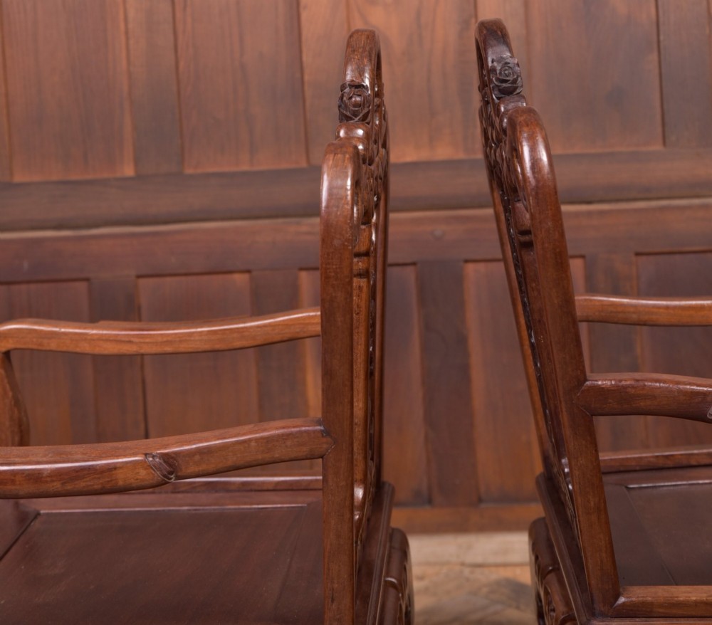A pair of dark warm brown Chinese hardwood armchairs featuring intricately carved floral back splats, openwork scroll aprons, and sculpted legs. View XI