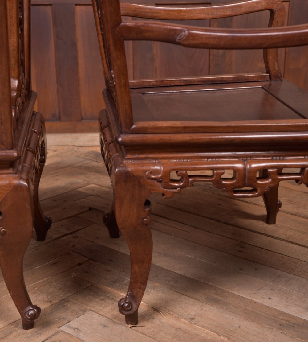 A pair of dark warm brown Chinese hardwood armchairs featuring intricately carved floral back splats, openwork scroll aprons, and sculpted legs. View XII