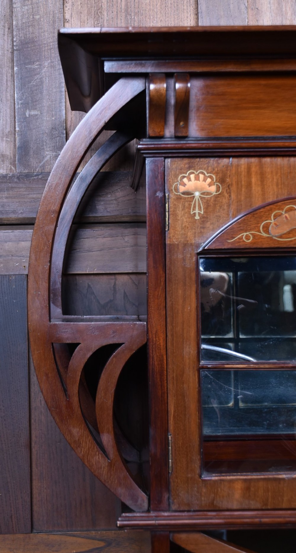 An Art Nouveau dark mahogany display cabinet featuring botanical inlay motifs, glazed upper doors, a central mirrored recess, a single drawer, and curved side brackets. View IX