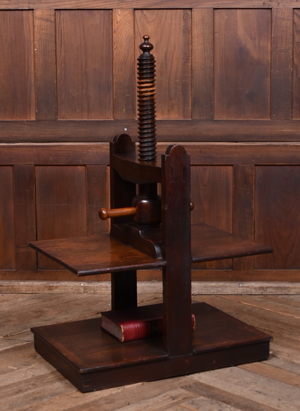 A Victorian dark oak wooden book press featuring a large central hand-turned screw mechanism and solid platen shelves.
