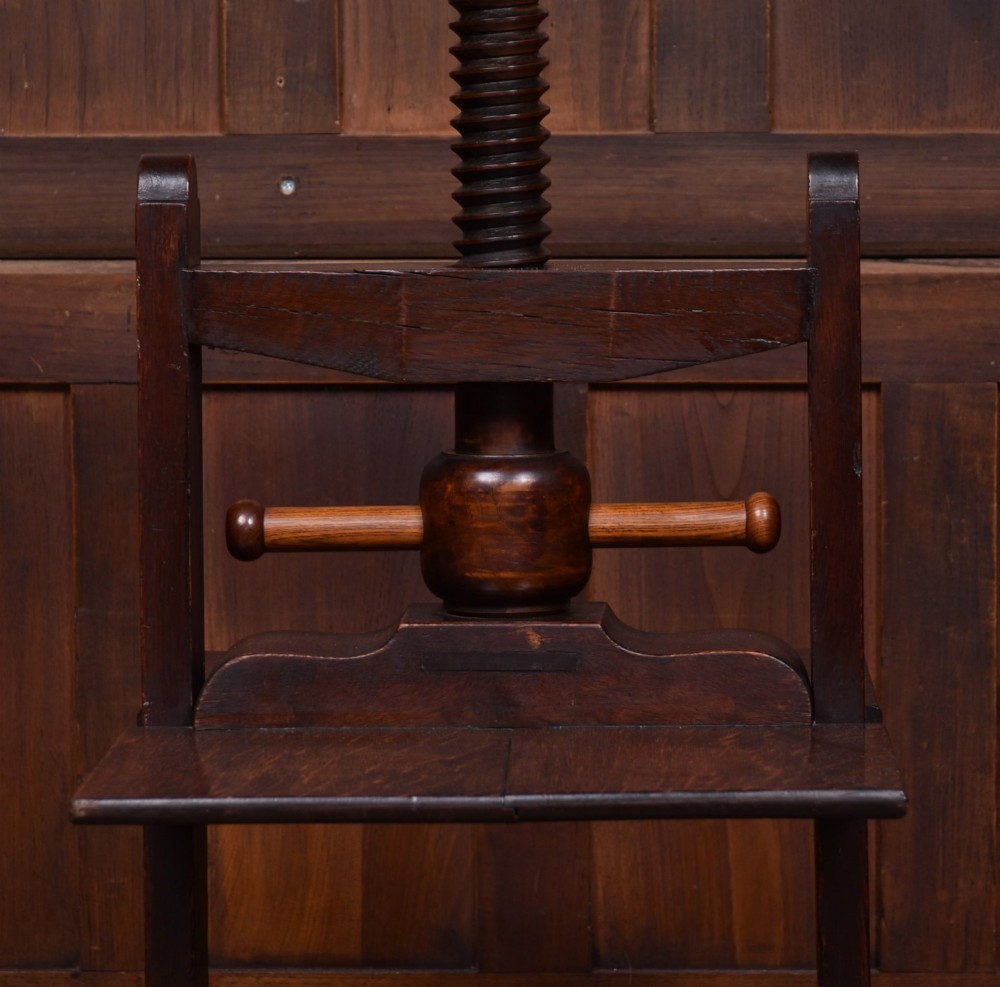 A Victorian dark oak wooden book press featuring a large central hand-turned screw mechanism and solid platen shelves. View VI