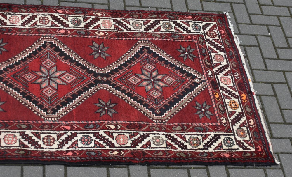 A long handwoven wool runner rug featuring five central diamond medallions on a dark red ground with geometric borders. View II
