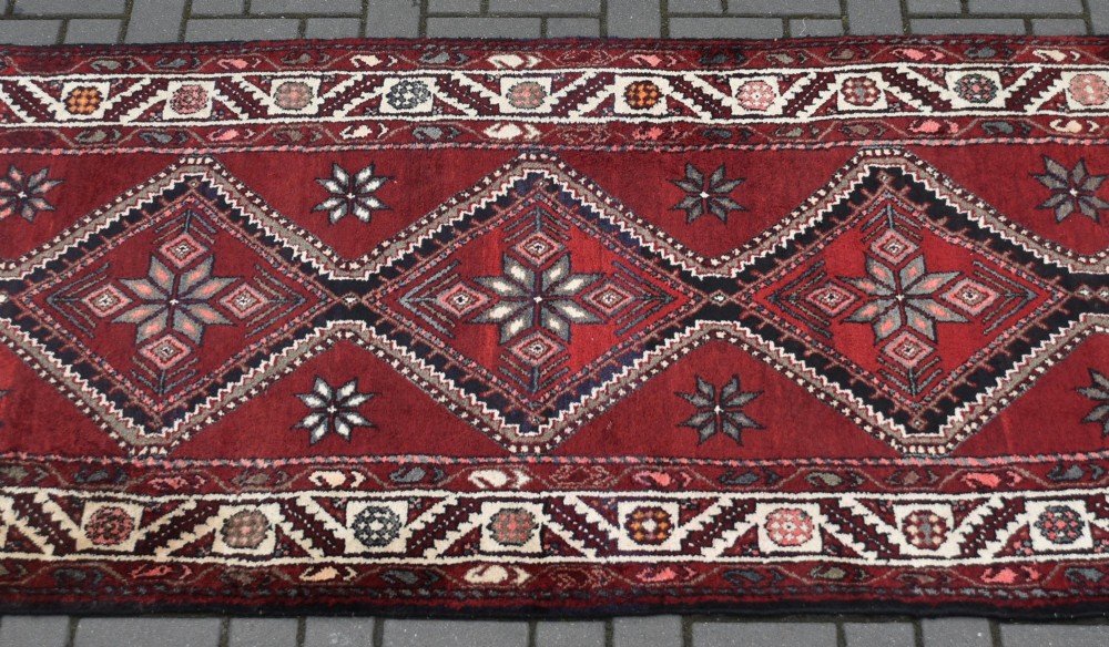 A long handwoven wool runner rug featuring five central diamond medallions on a dark red ground with geometric borders. View III