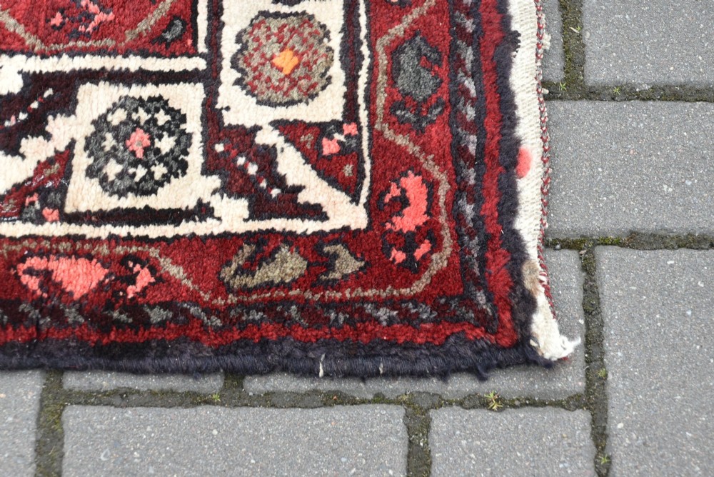 A long handwoven wool runner rug featuring five central diamond medallions on a dark red ground with geometric borders. View V
