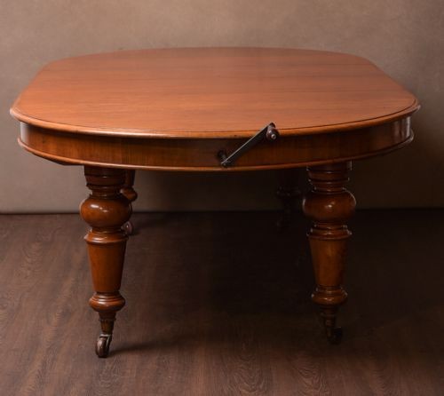 A Victorian mahogany extendable dining table featuring turned legs on brass castors, rounded tabletop corners, and an exposed metal winding crank handle.