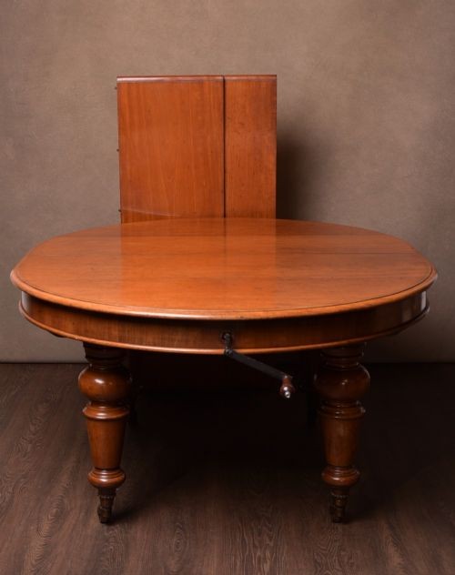 A Victorian mahogany extendable dining table featuring turned legs on brass castors, rounded tabletop corners, and an exposed metal winding crank handle. View II