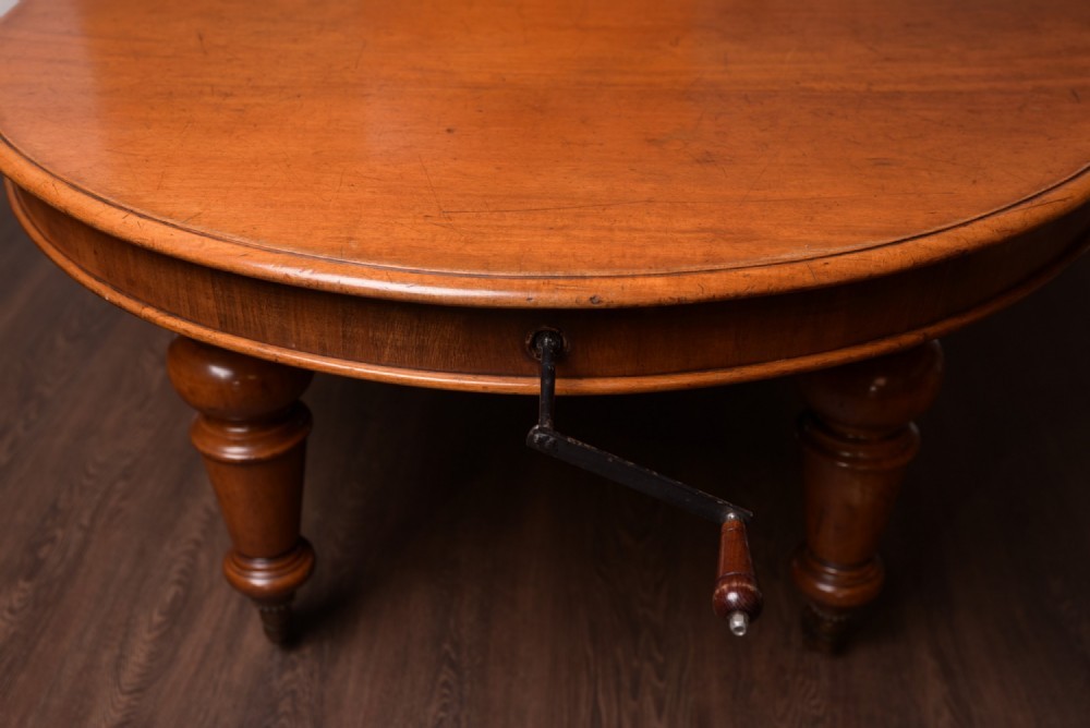 A Victorian mahogany extendable dining table featuring turned legs on brass castors, rounded tabletop corners, and an exposed metal winding crank handle. View III
