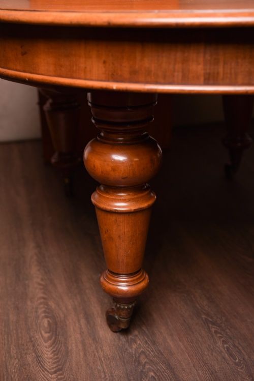 A Victorian mahogany extendable dining table featuring turned legs on brass castors, rounded tabletop corners, and an exposed metal winding crank handle. View IV