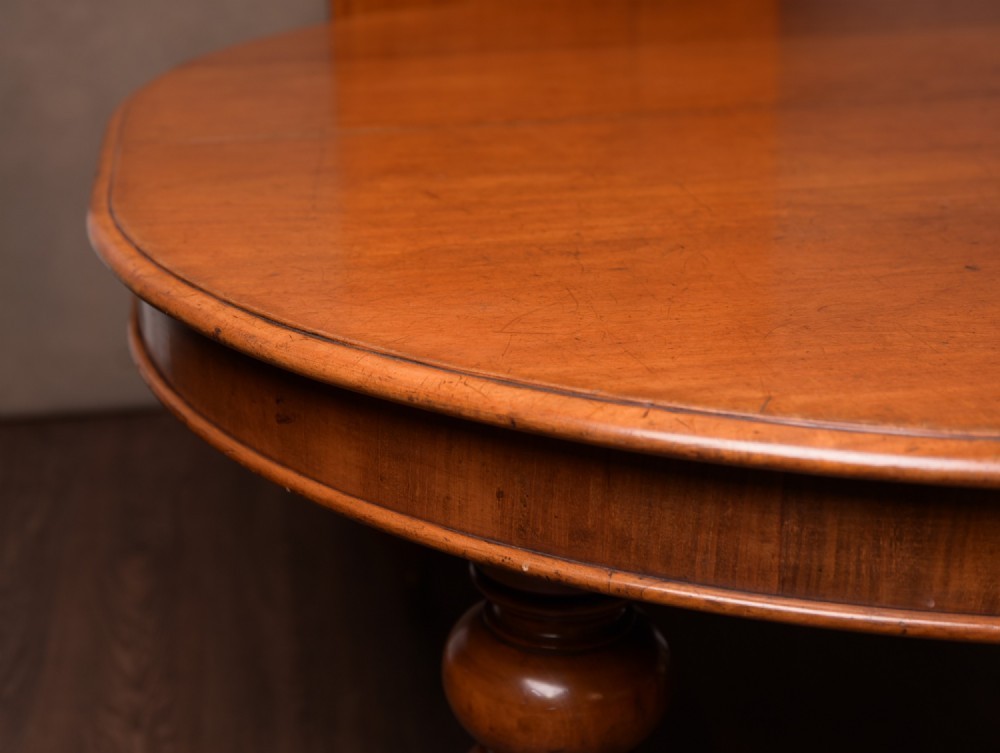 A Victorian mahogany extendable dining table featuring turned legs on brass castors, rounded tabletop corners, and an exposed metal winding crank handle. View VI