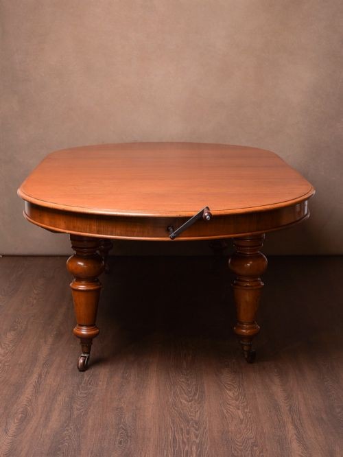 A Victorian mahogany extendable dining table featuring turned legs on brass castors, rounded tabletop corners, and an exposed metal winding crank handle. View VIII