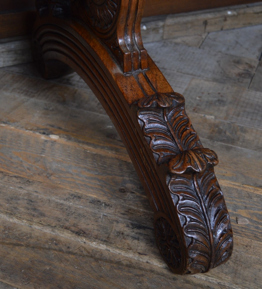 A Victorian carved padauk wood library table featuring three frieze drawers and an intricate carved trestle base with an arched central stretcher. View V
