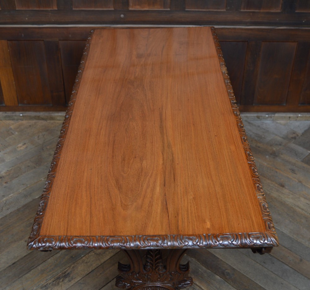 A Victorian carved padauk wood library table featuring three frieze drawers and an intricate carved trestle base with an arched central stretcher. View XII