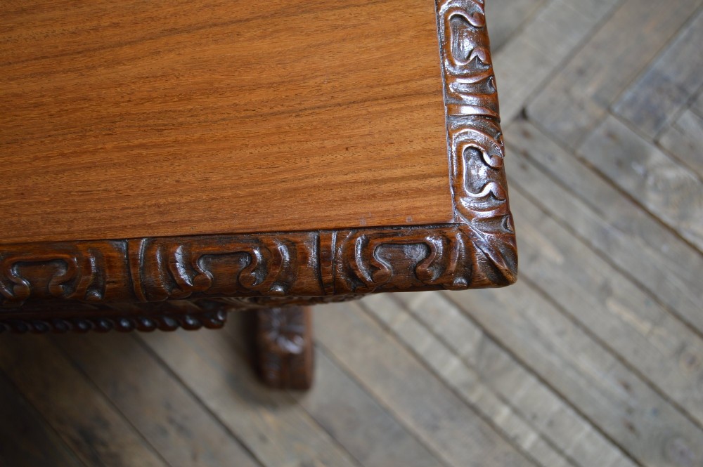 A Victorian carved padauk wood library table featuring three frieze drawers and an intricate carved trestle base with an arched central stretcher. View XIII