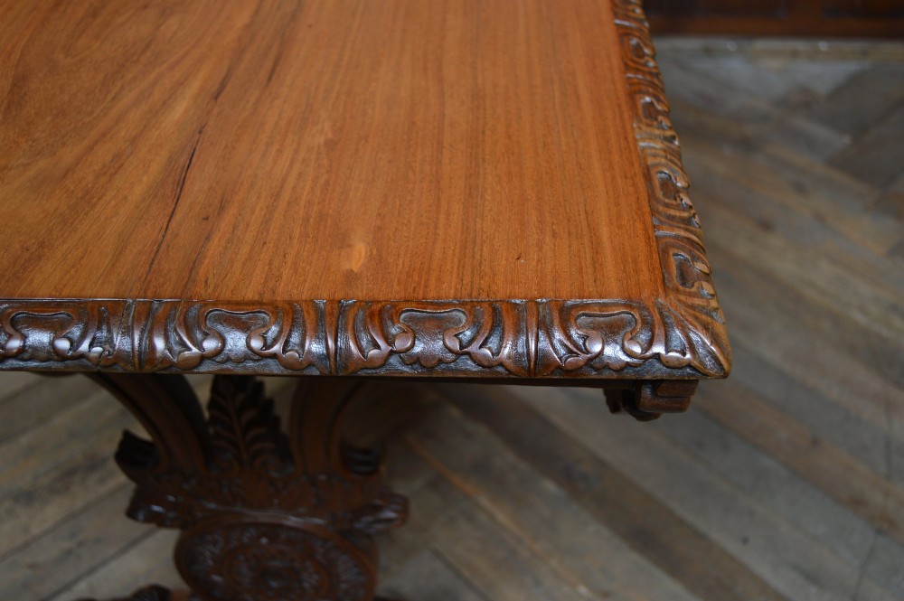 A Victorian carved padauk wood library table featuring three frieze drawers and an intricate carved trestle base with an arched central stretcher. View XIV